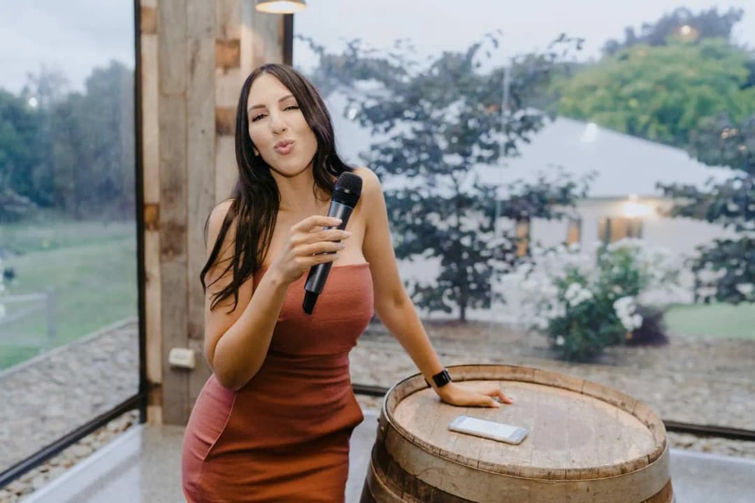Woman holding a microphone beside a wooden barrel and large reception window