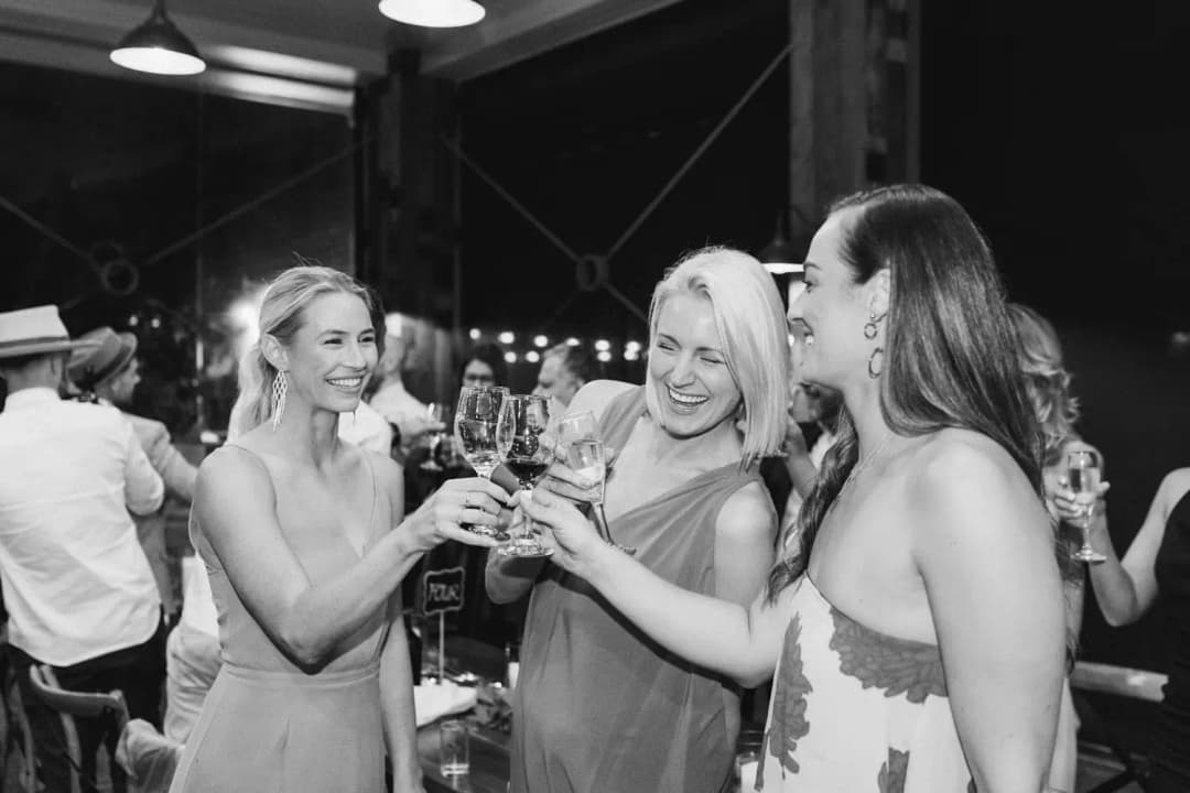 Black and white photograph of women raising glasses together at the reception