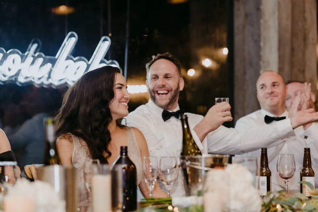 Bride and groom laughing together with a groomsman at the reception table