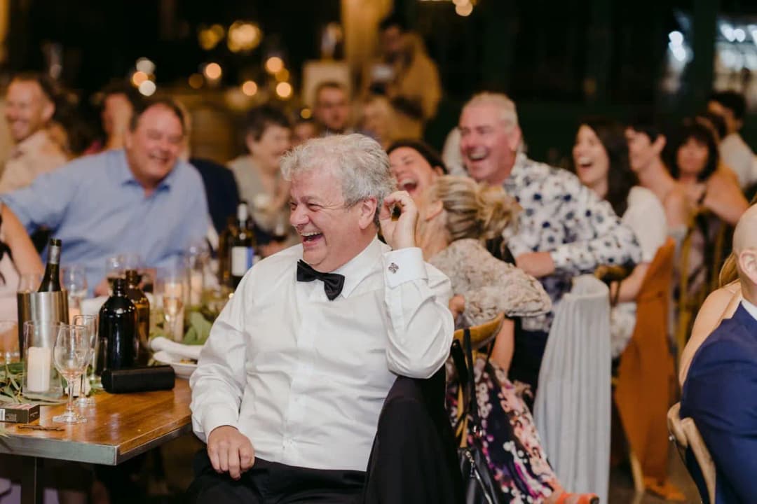 Grey-haired guest laughing while seated among wedding guests
