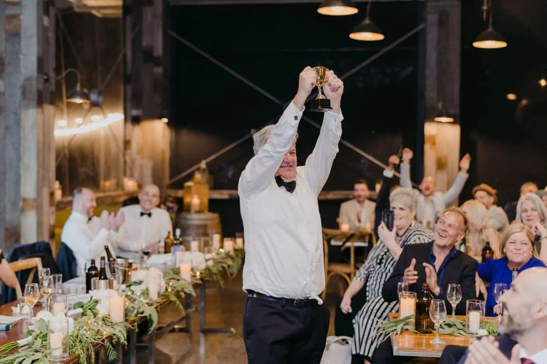 Guest raising both hands above his head while others cheer around the reception table
