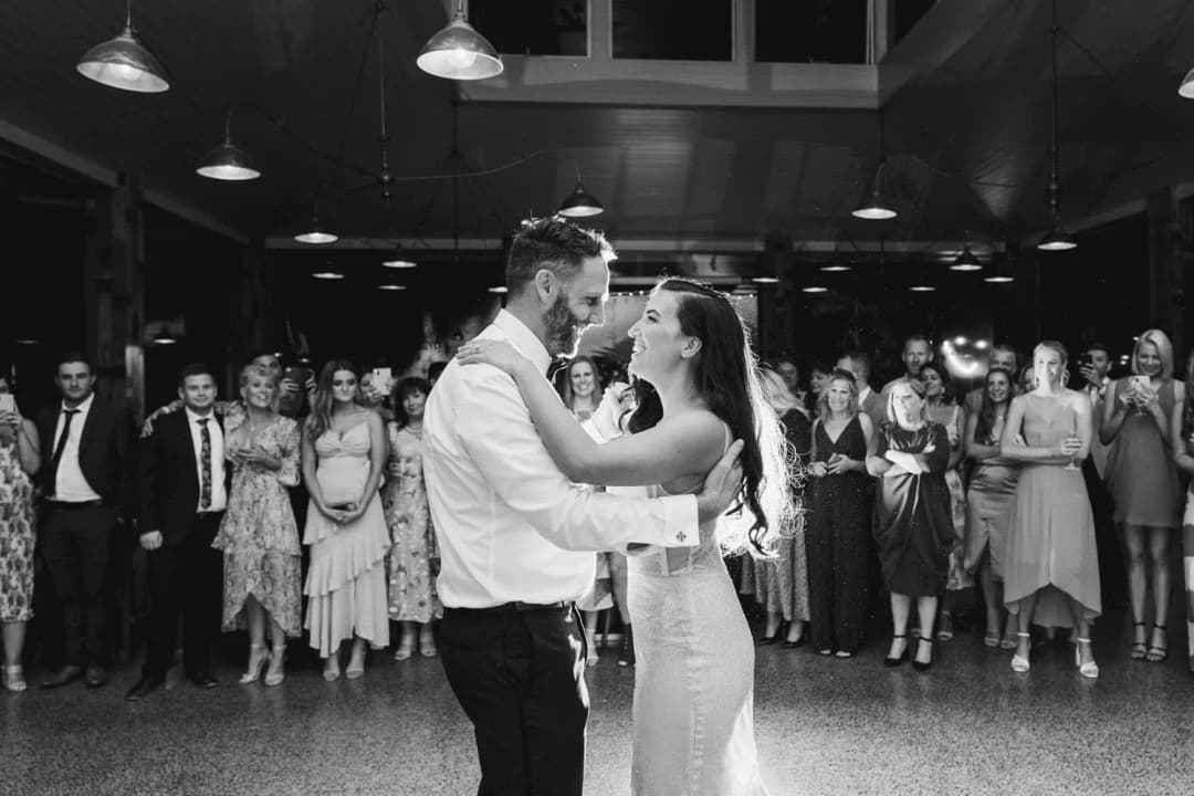 Black and white photograph of the bride and groom dancing as guests watch