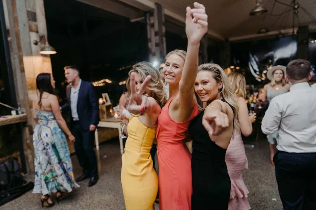 Three women laughing and raising their arms on the dance floor