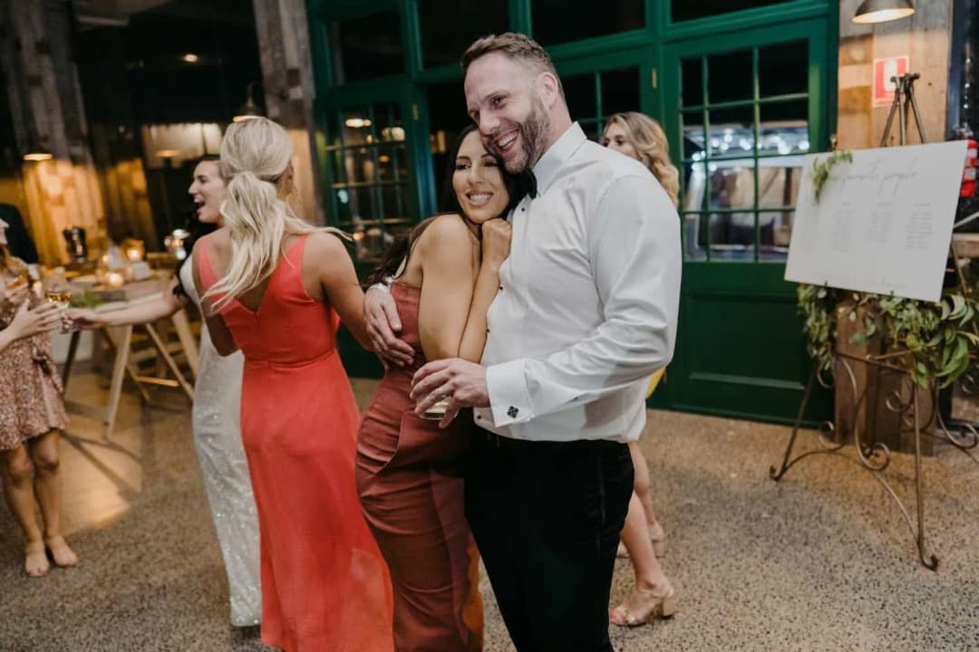 Groom dancing beside a smiling guest while holding a drink