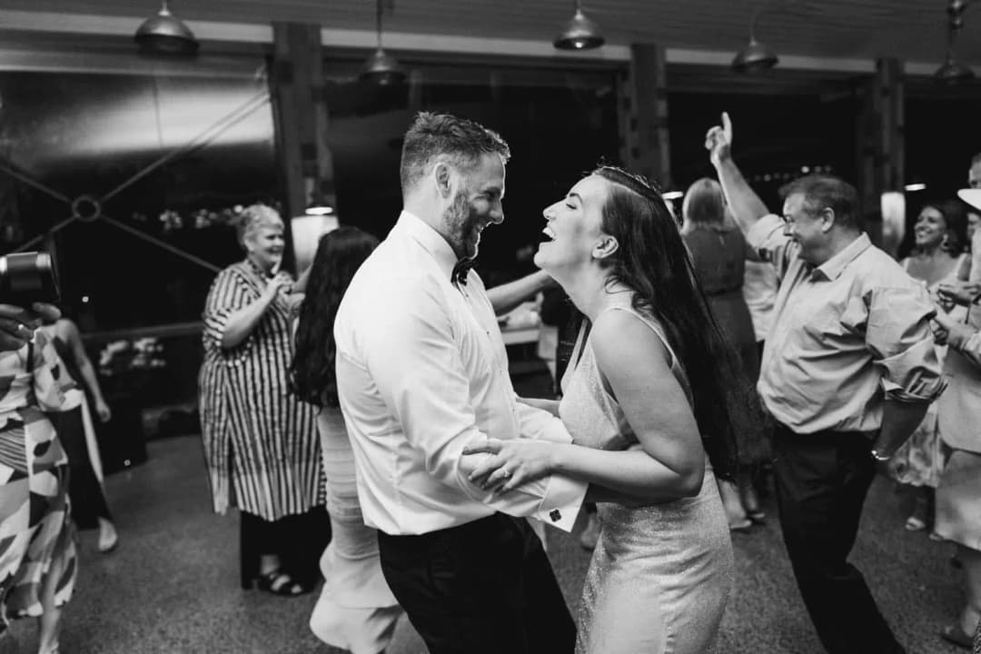Black and white photograph of the bride and groom laughing together on the dance floor