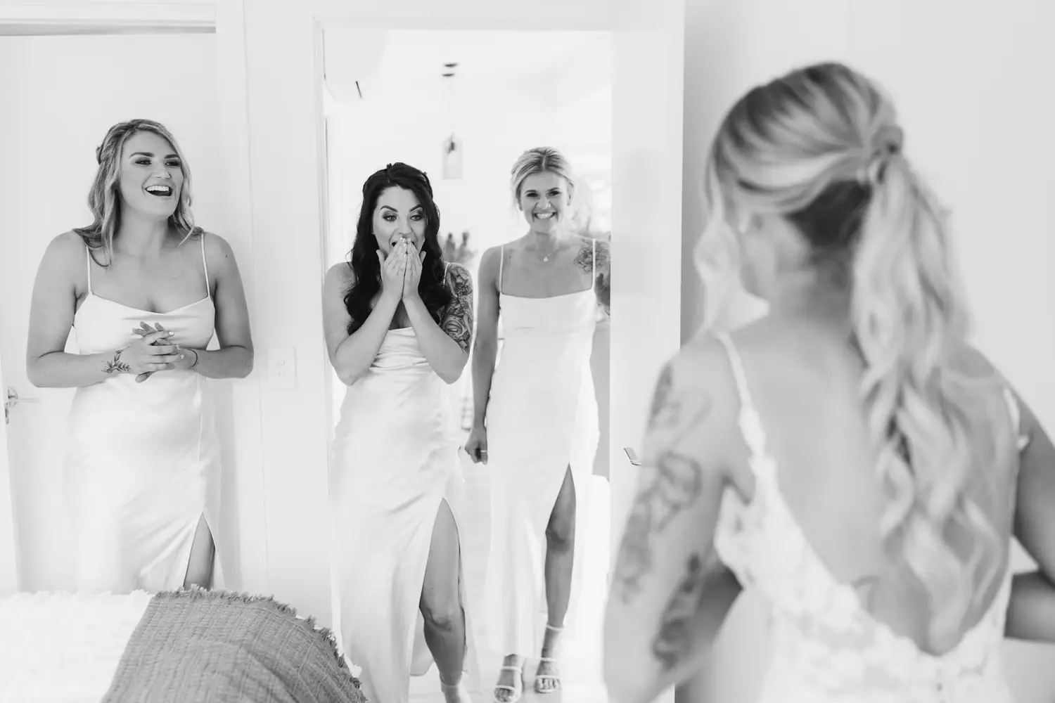 Black and white photograph of bridesmaids reacting to the bride's wedding dress.