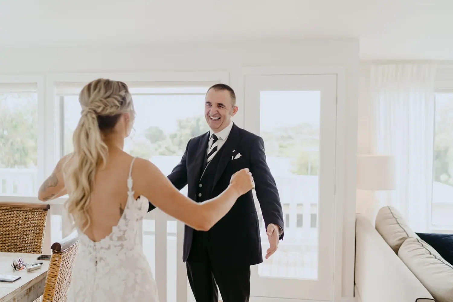 Bride approaches a smiling man in a suit in a bright room.