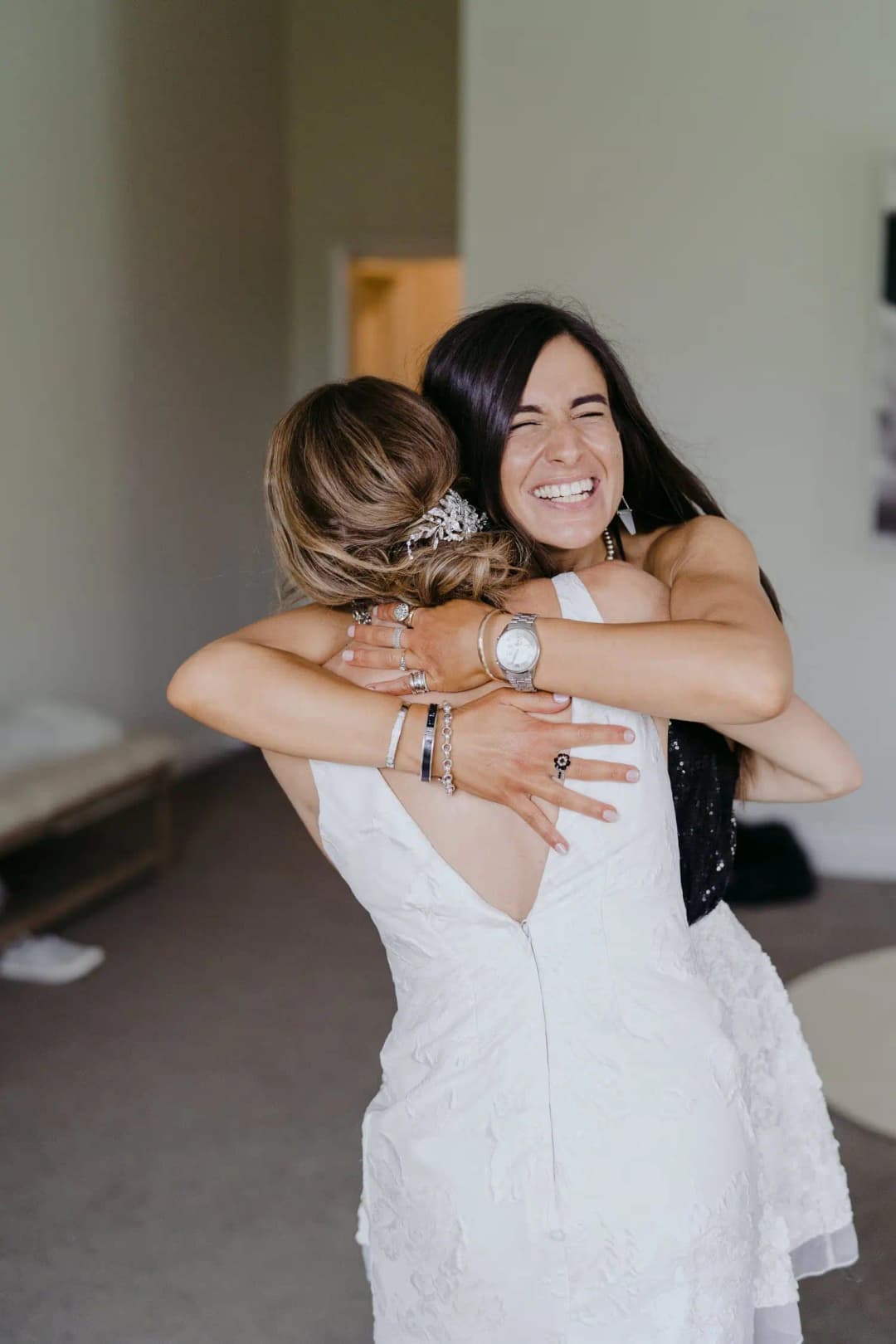 Bride and a woman embrace indoors.