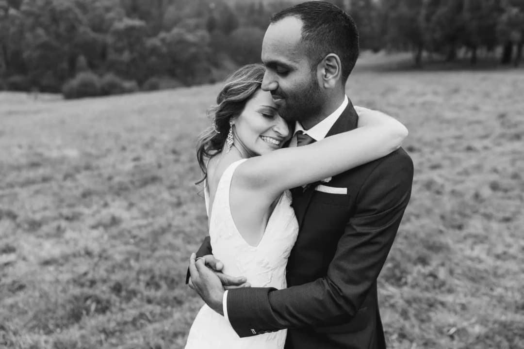 Black and white photograph of the groom kissing the bride's forehead in a field.