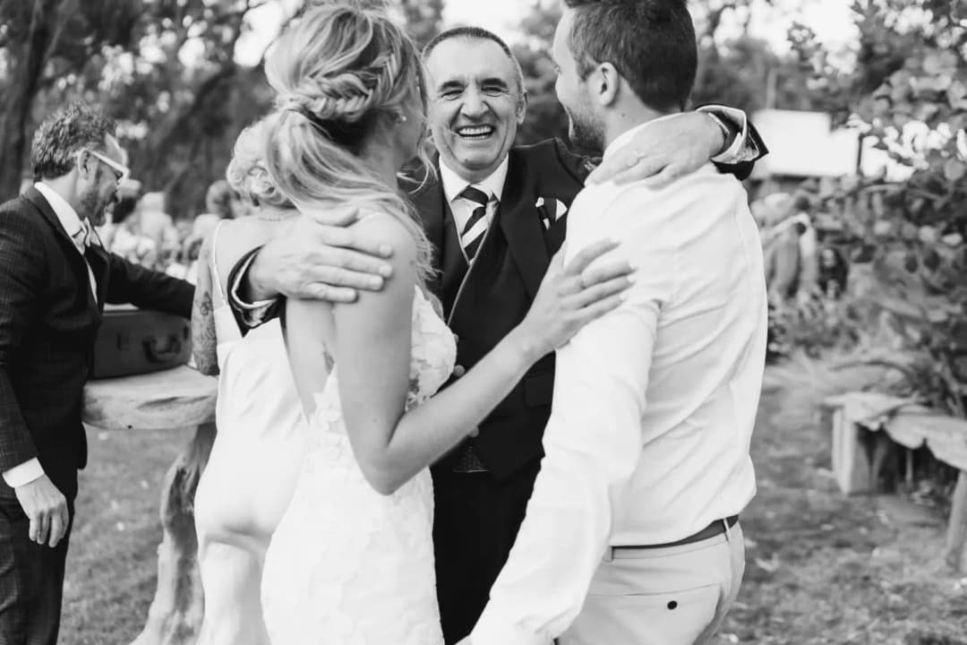Black and white photograph of an older man embracing the couple outdoors.