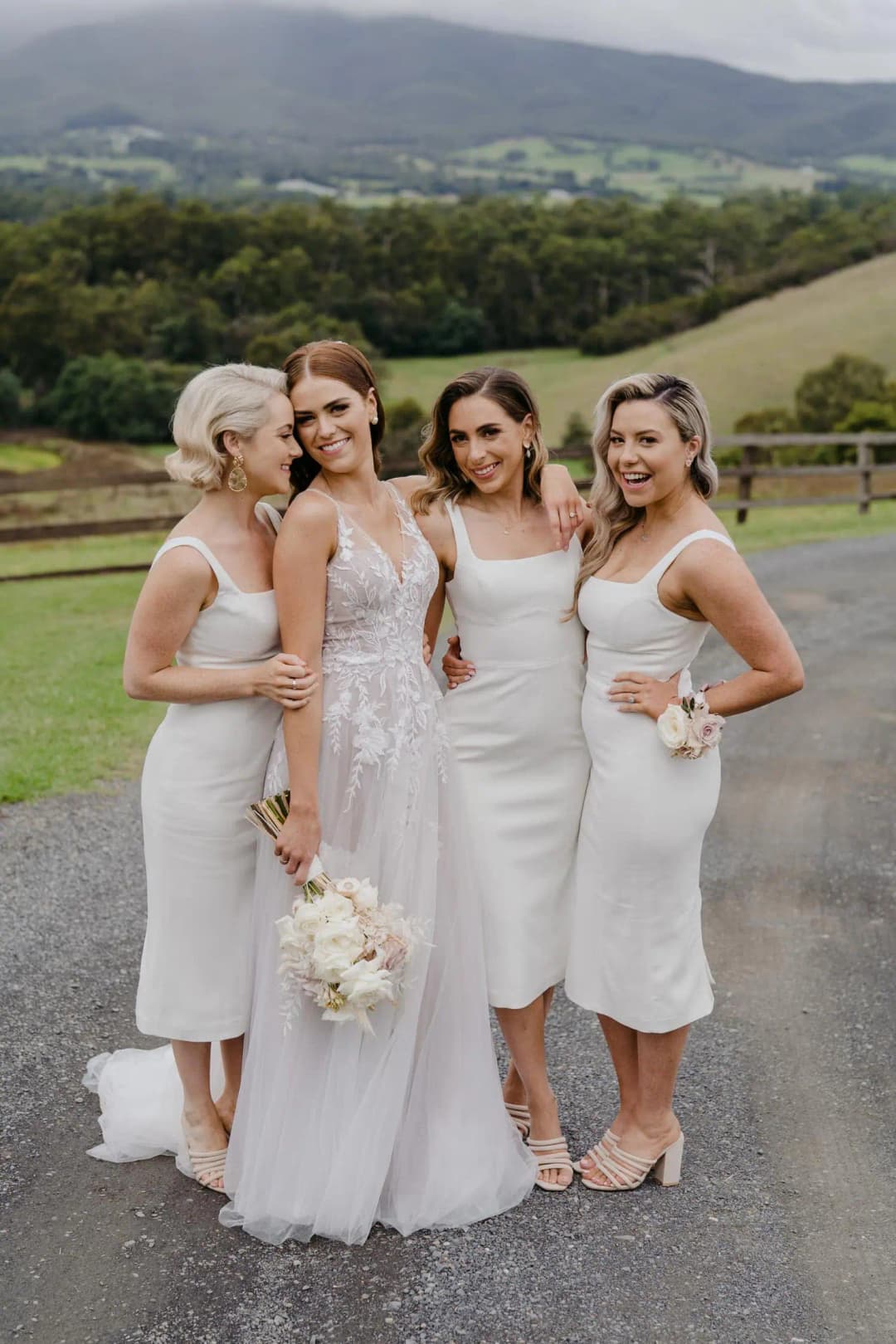 Bride and three bridesmaids pose on a road with rolling hills behind them.
