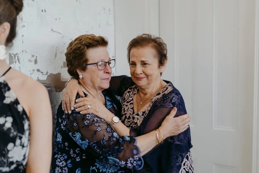 Two older women embrace in a bright room.