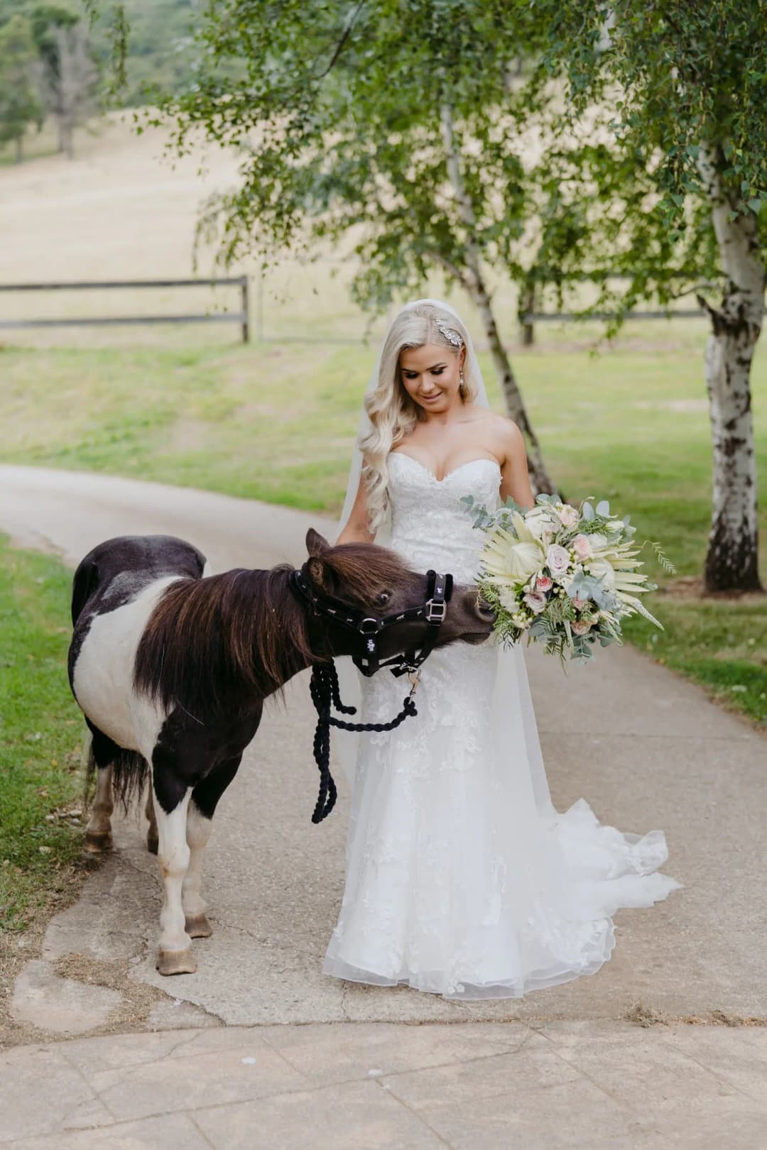 Bride holds a bouquet beside a black and white pony outdoors.