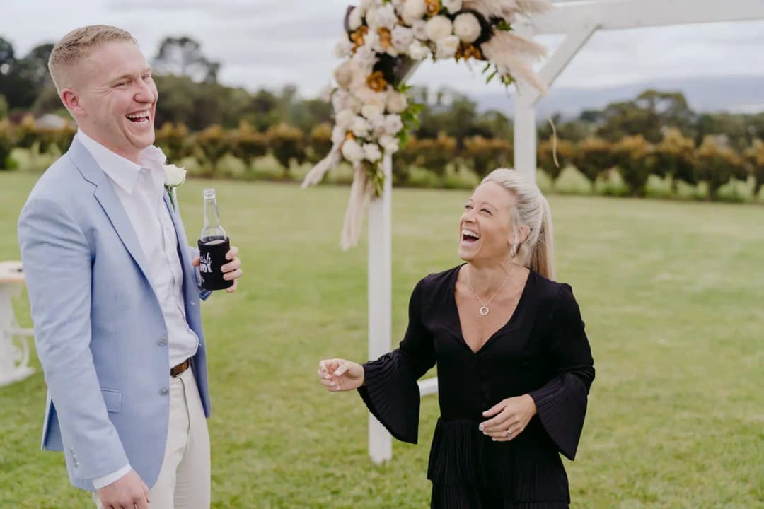 Man and an older woman laugh together beside the ceremony arch.