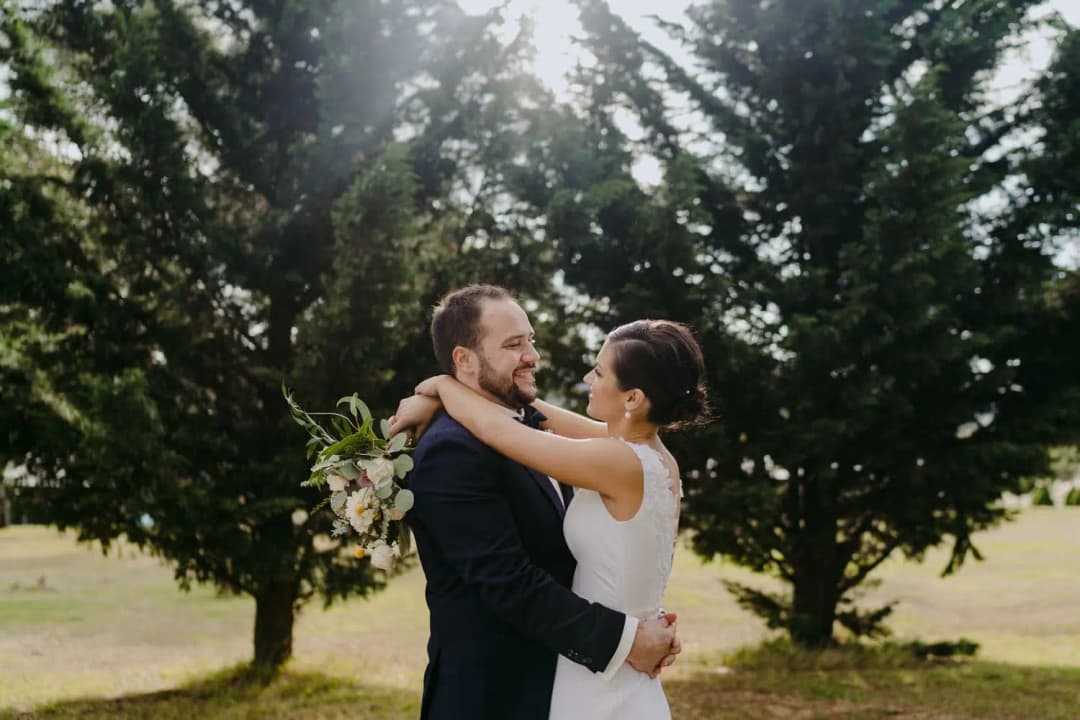Couple embraces on a lawn framed by two leafy trees.