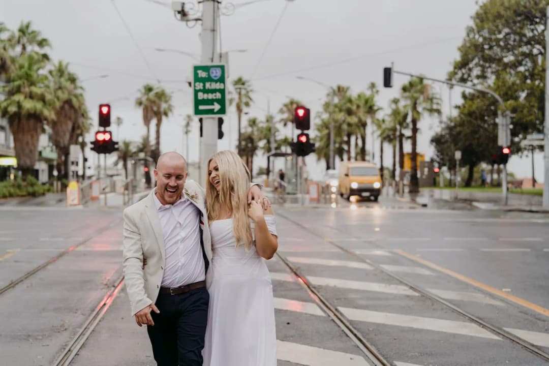 Couple laughs while standing beside a wet city intersection.