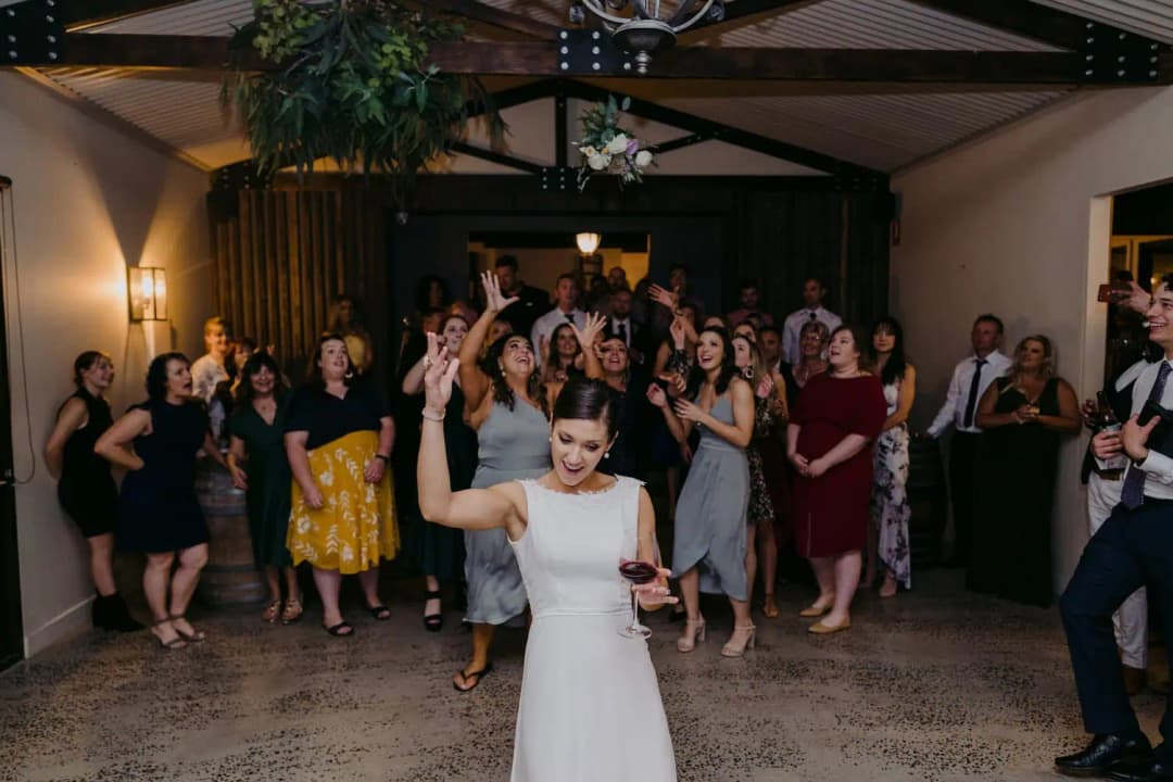 Bride raises an arm in front of guests gathered for the bouquet toss.
