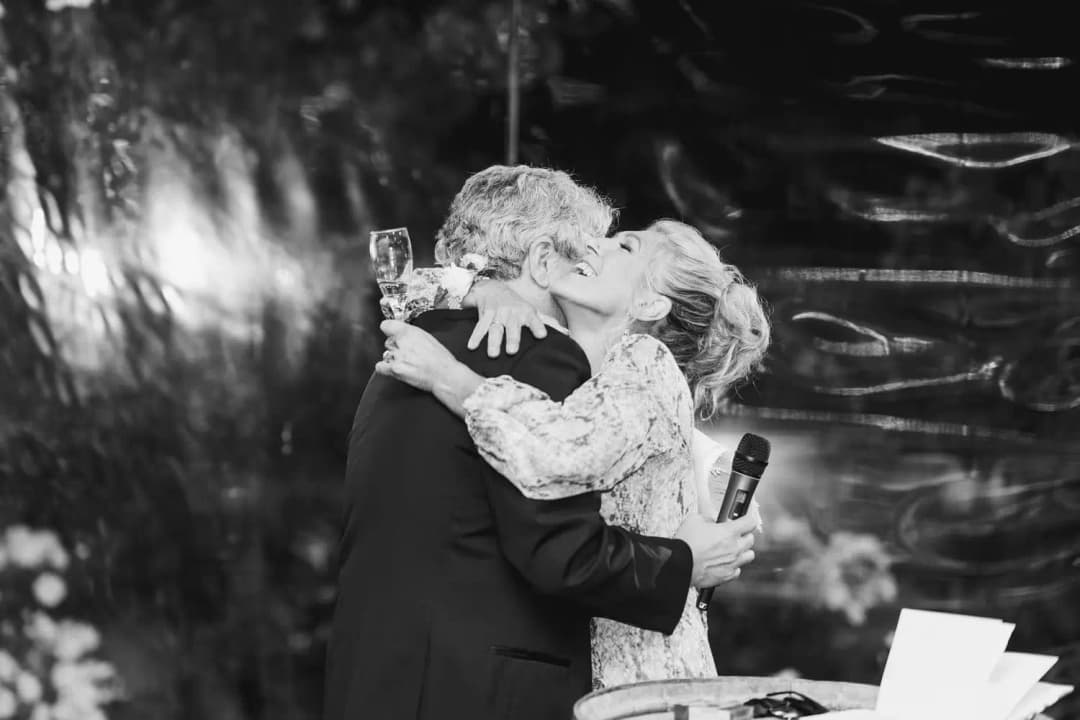 Black and white photograph of two older guests embracing after a speech.