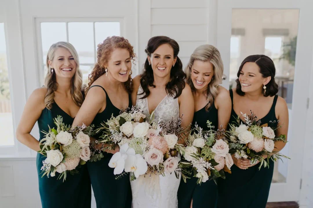 Bride and four bridesmaids smile together holding white and pink bouquets.