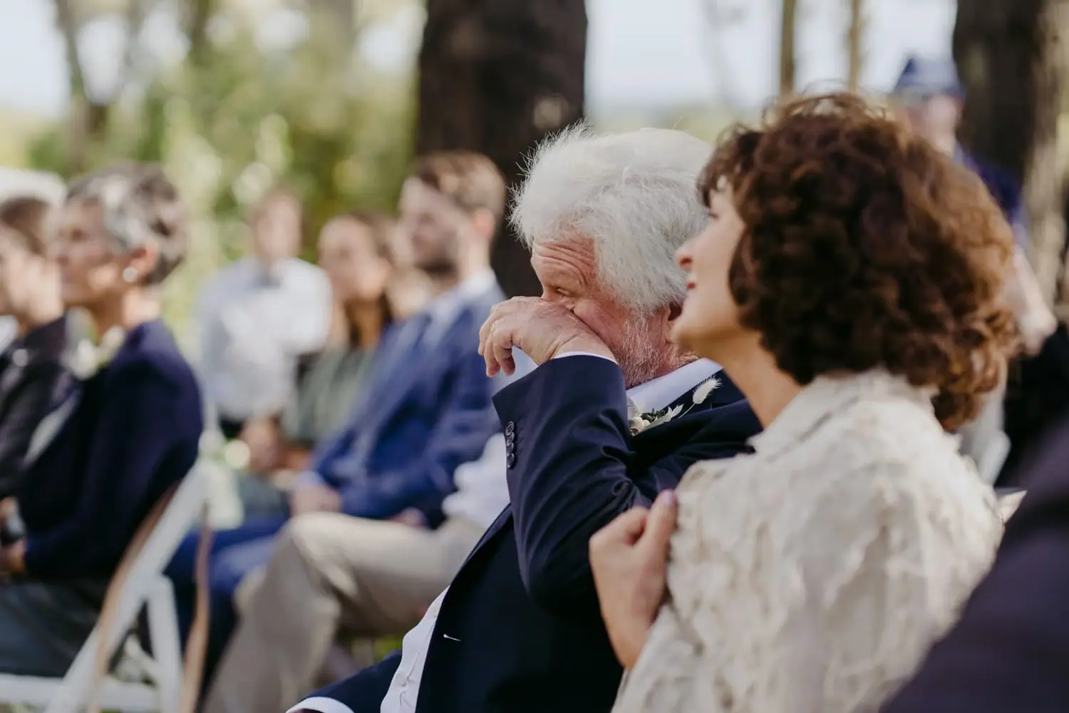 Older guest wipes his eye while seated at the outdoor ceremony.