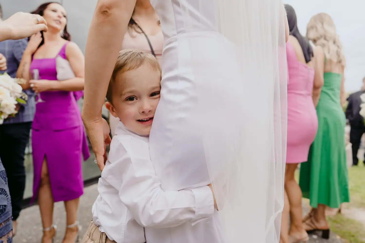 Small child peeks around the bride's dress among wedding guests.