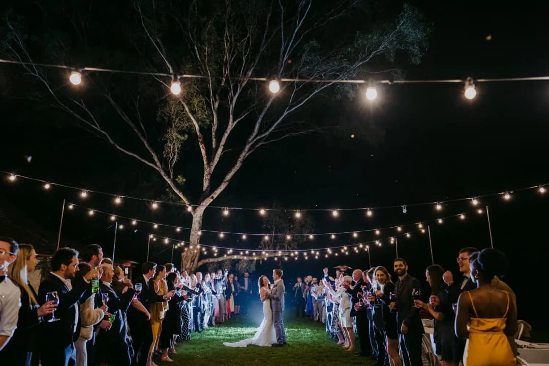Guests form a circle beneath outdoor string lights around the couple at night.