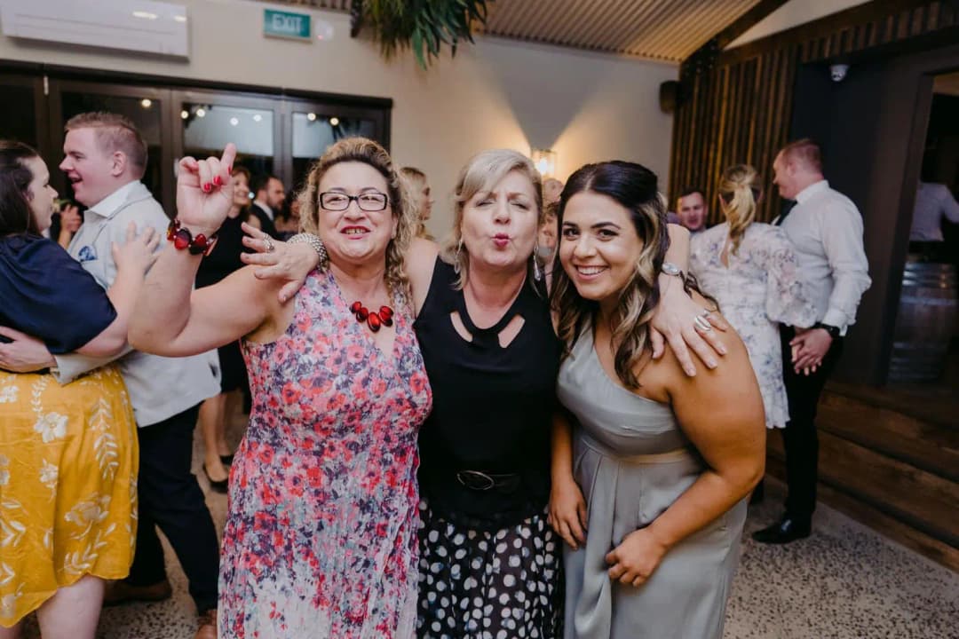 Three women pose together on the reception dance floor.