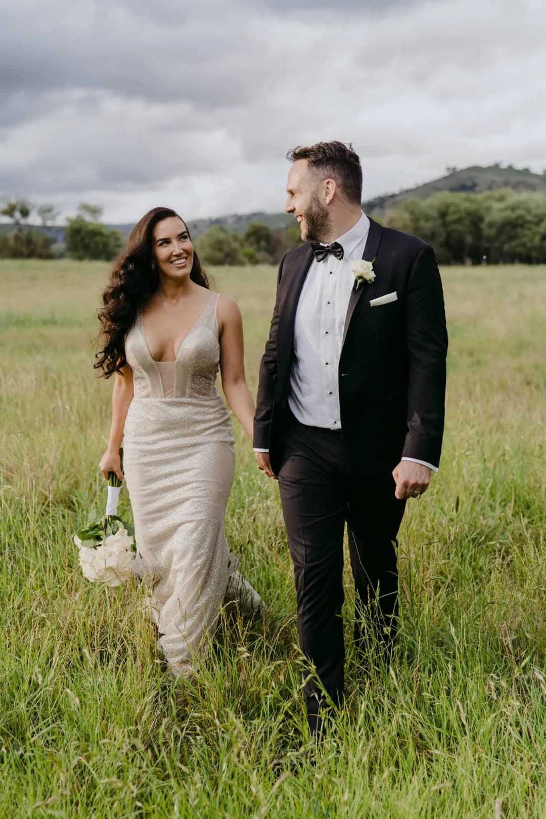 Couple smiles at each other while walking through long grass.