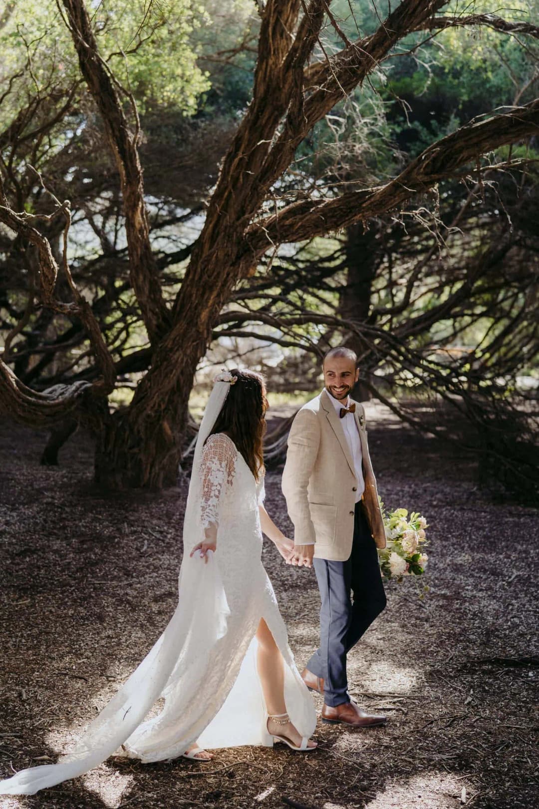 Couple walks beneath spreading trees along a shaded path.