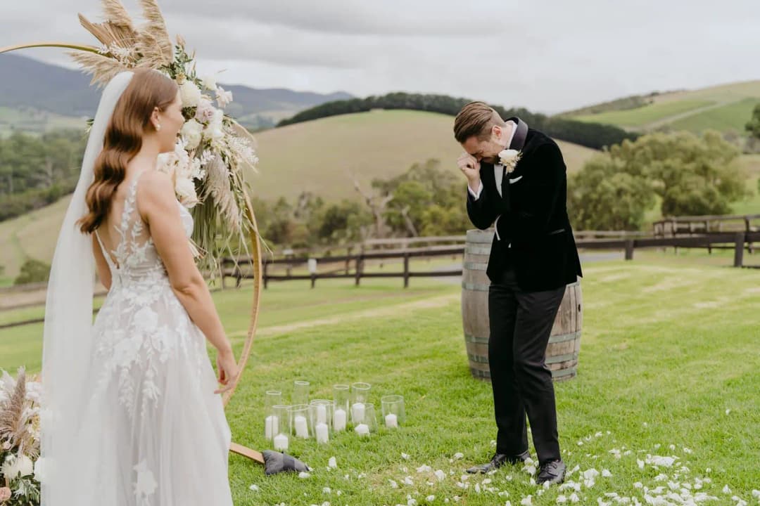 Groom wipes his eye as the bride faces him at the outdoor ceremony.