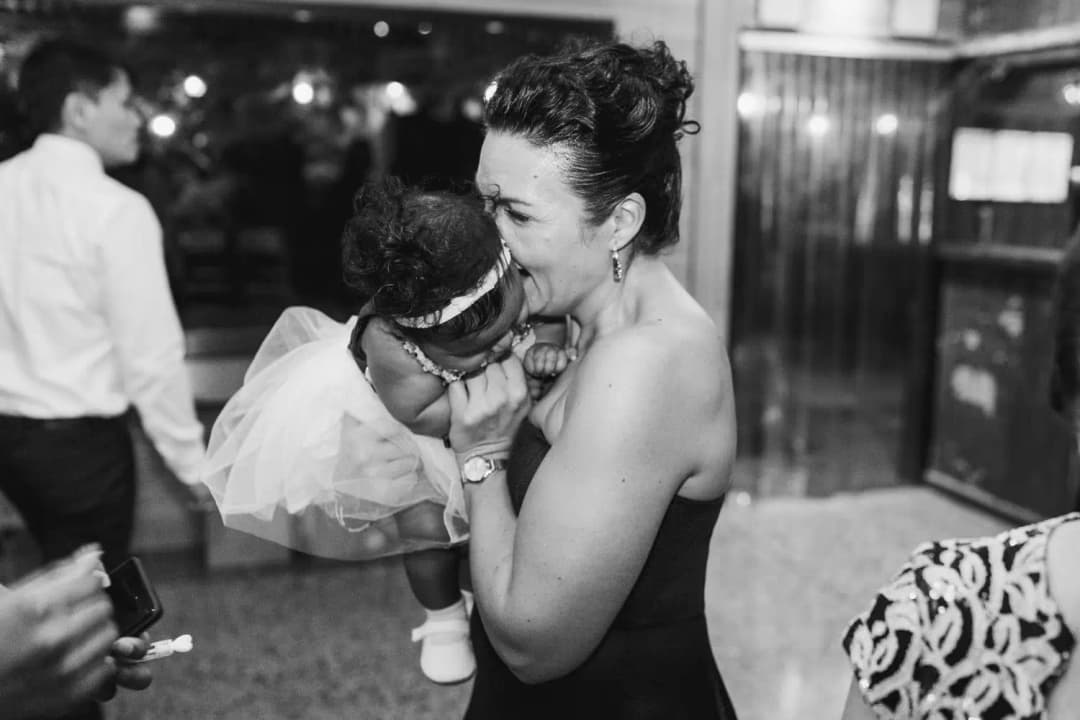 Black and white photograph of a woman holding and kissing a small child at the reception.