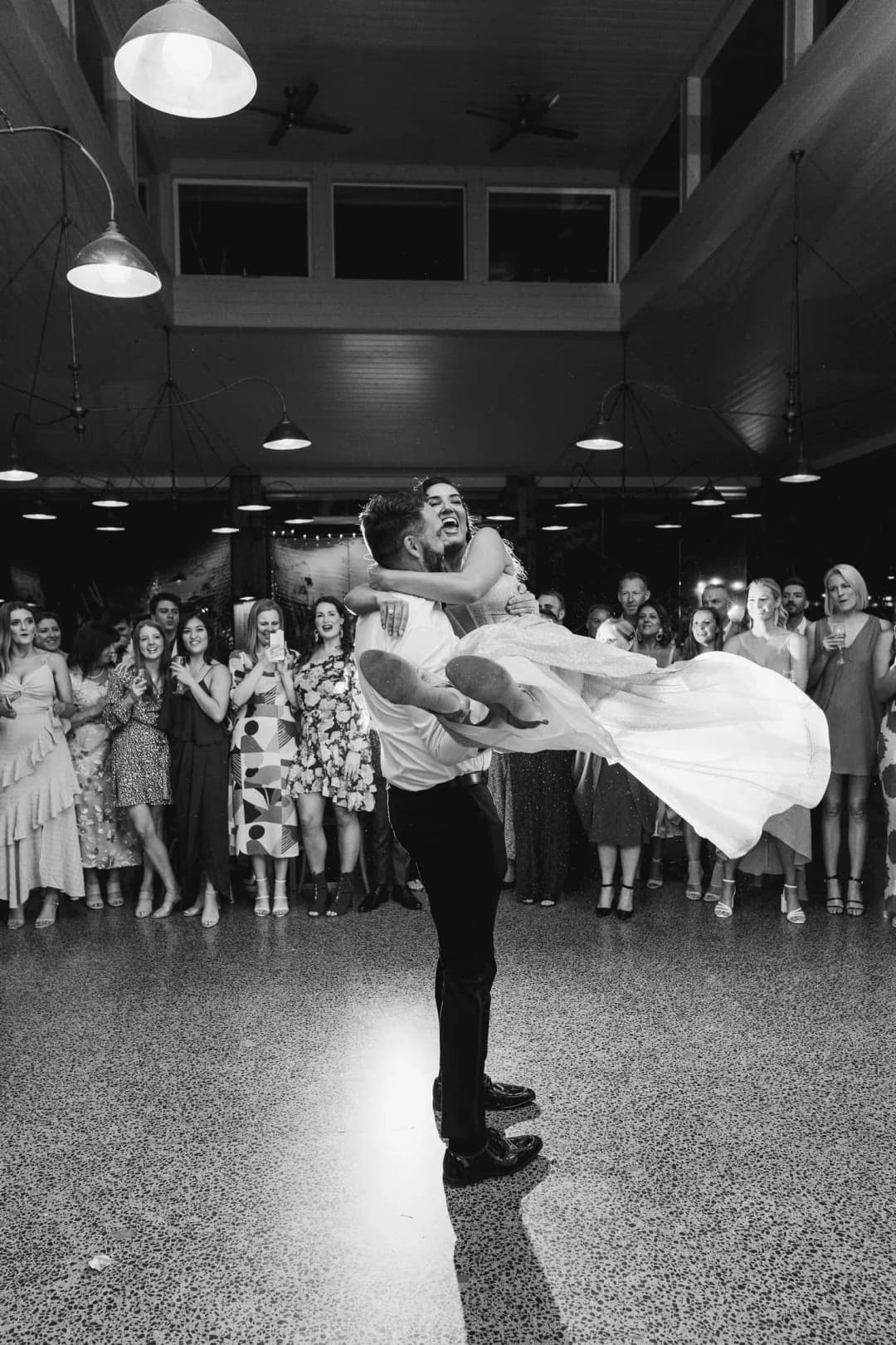 Black and white photograph of the groom lifting the bride on the dance floor.