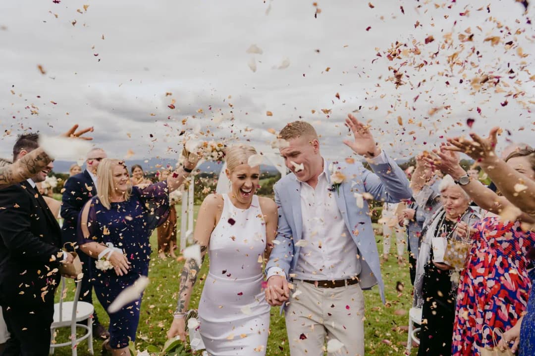 Couple walks through a shower of confetti thrown by guests.