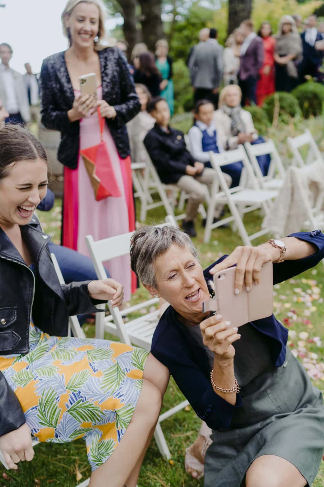 Guests laugh and shield their faces beside the ceremony chairs.