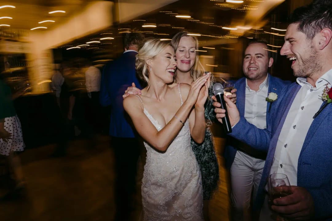 Bride and guests laugh together with drinks on the dance floor.
