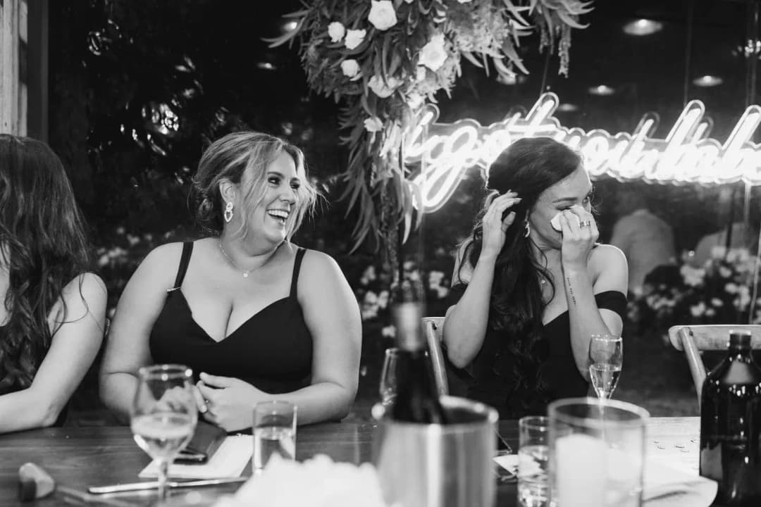 Black and white photograph of two women reacting to a speech at the reception table.