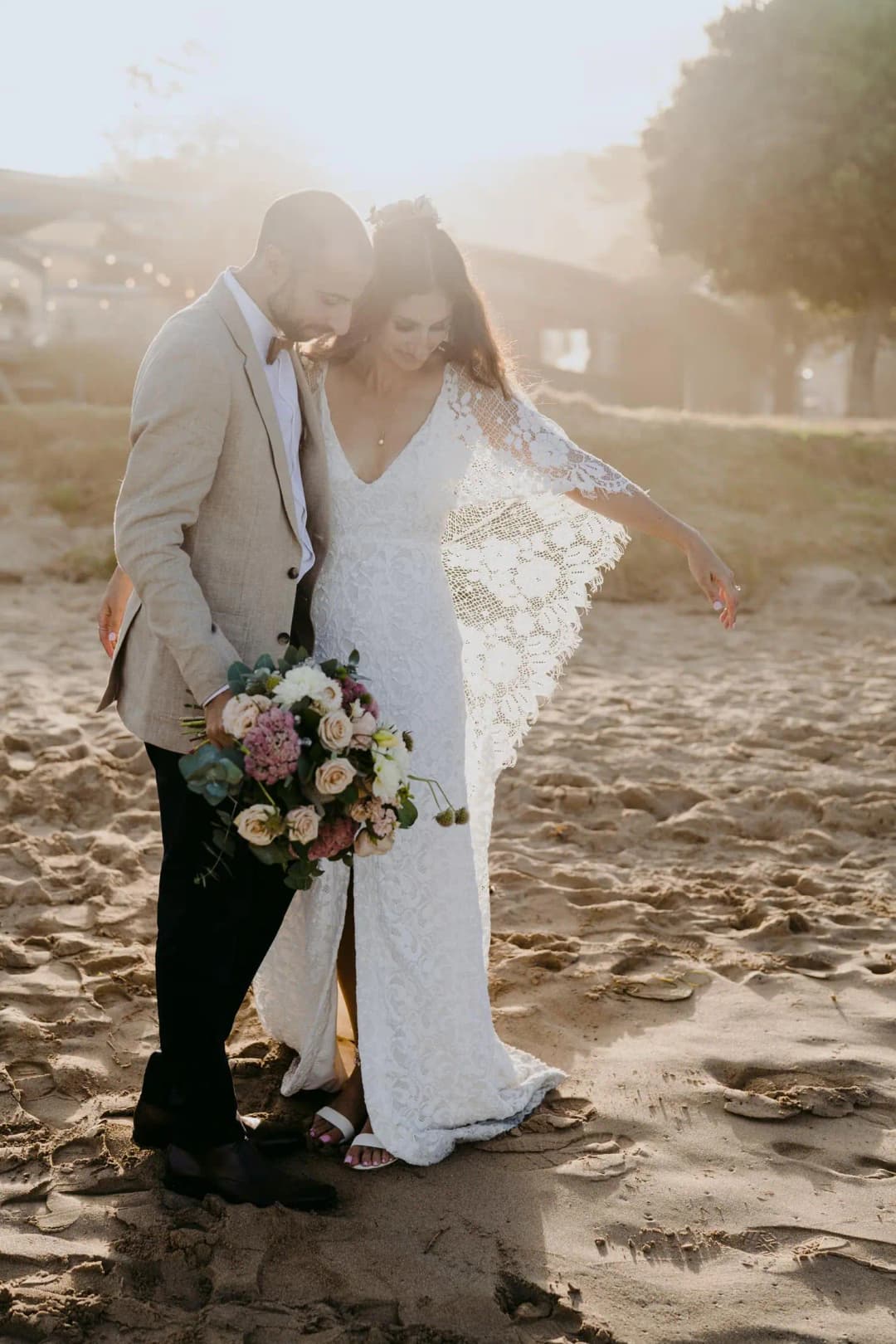 Couple kisses on the beach with low sunlight shining through the bride's veil.