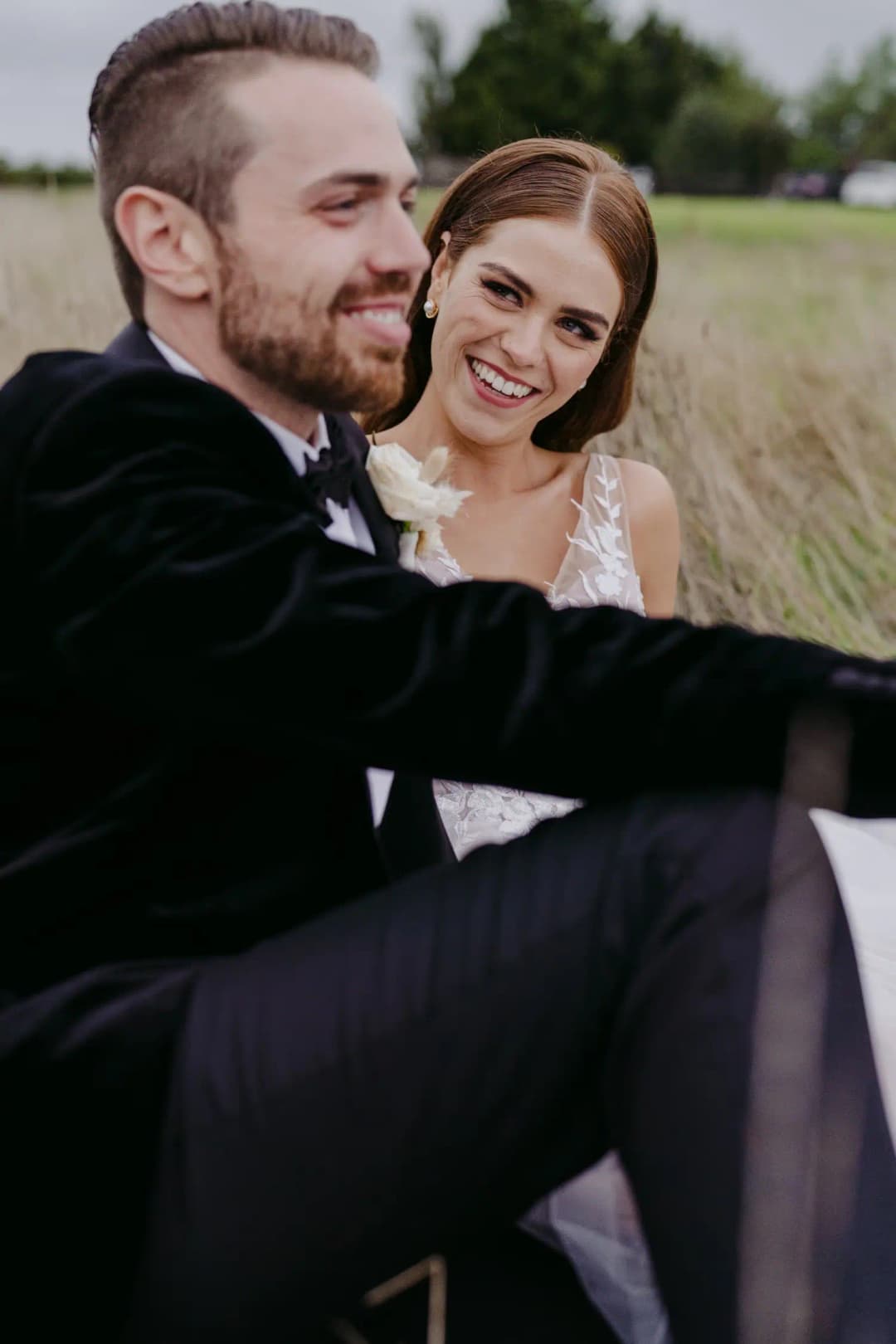 Couple sits close together in a grassy field.