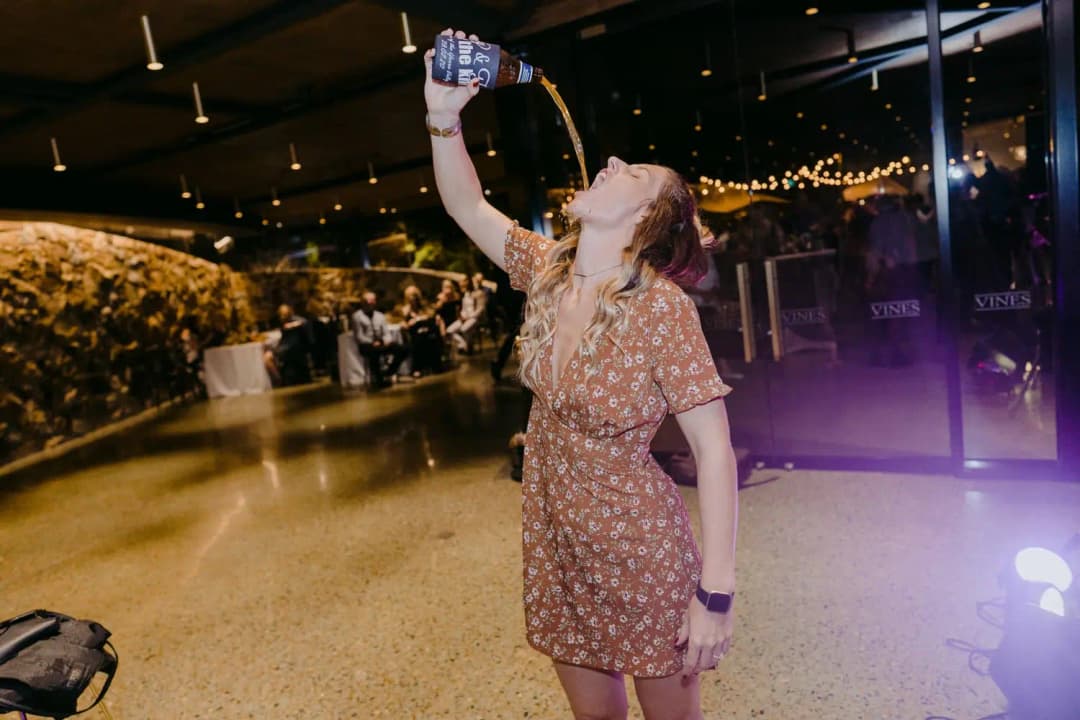 Guest pours a drink toward her mouth from a raised bottle on the dance floor.