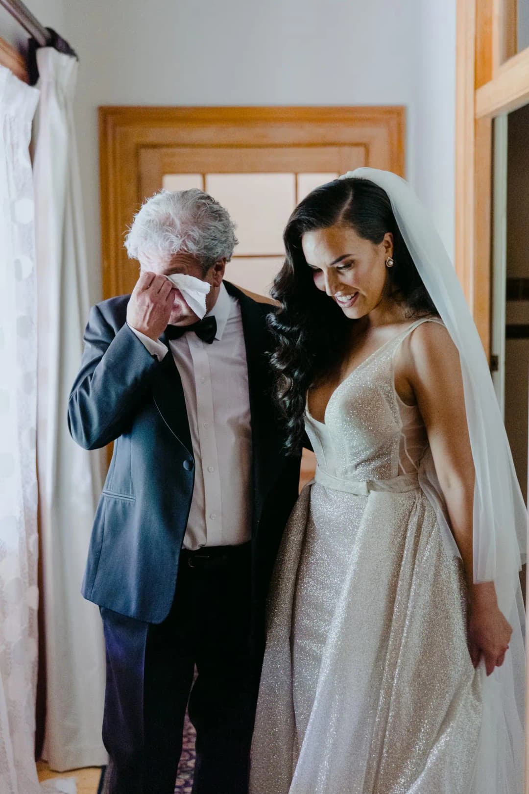 Older man wipes his eye while standing beside the bride in a doorway.