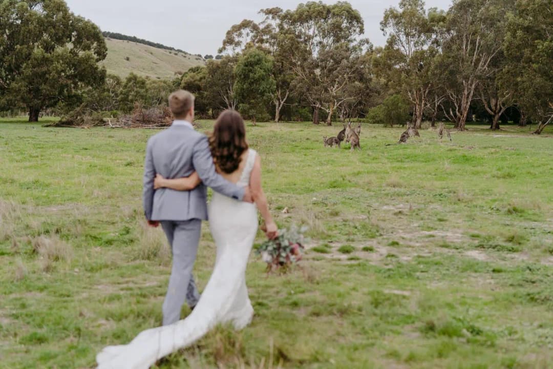 Rear view of the couple walking arm in arm across a grassy field.