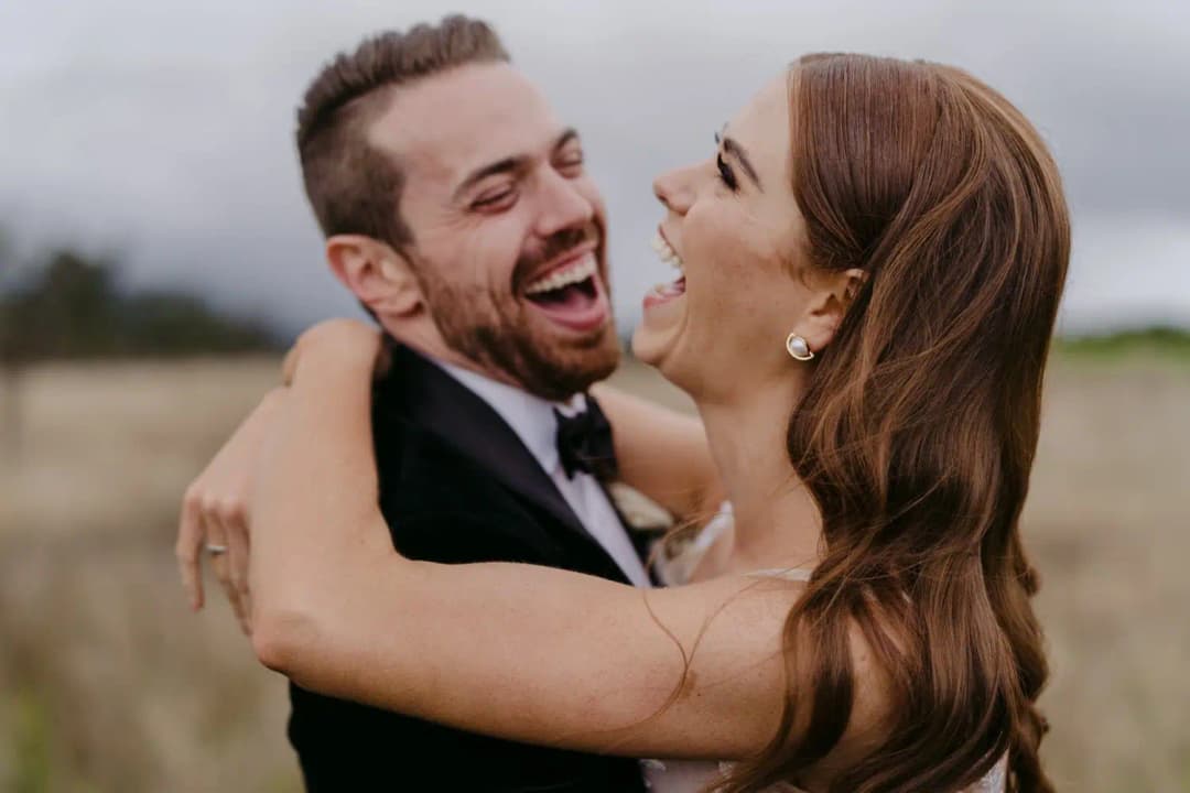 Close portrait of the couple laughing together in a field.