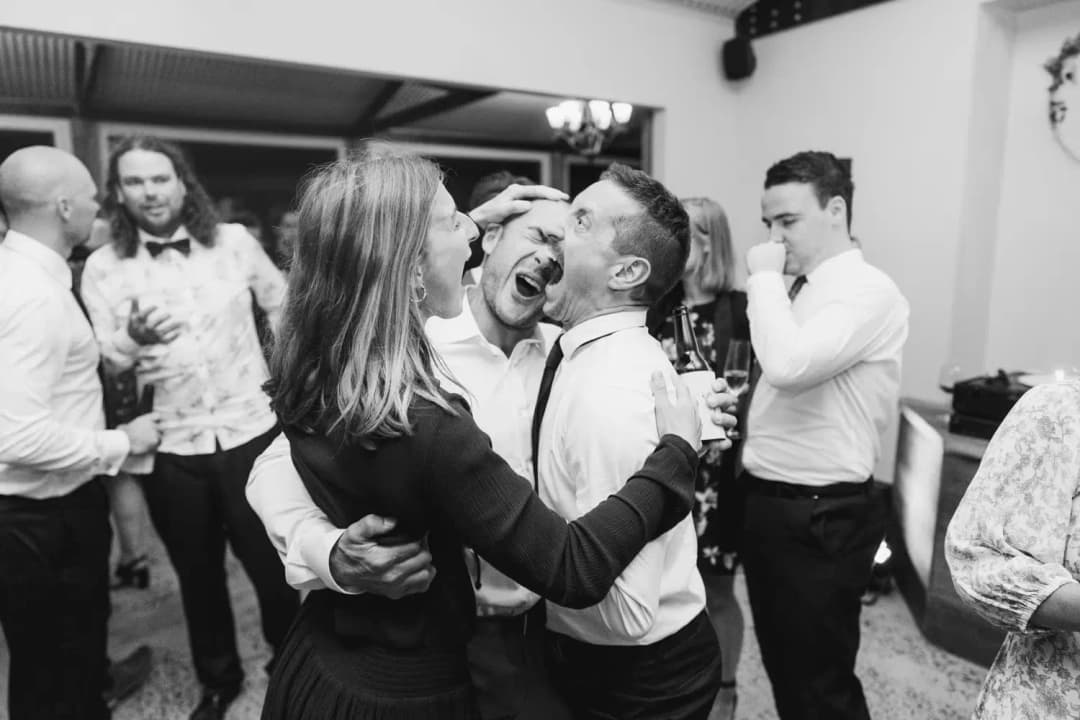 Black and white photograph of guests laughing and embracing on the dance floor.