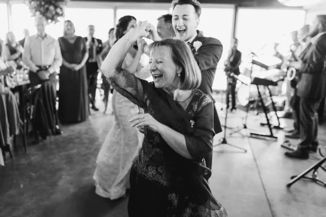 Black and white photograph of a man twirling a laughing guest beside the live band.