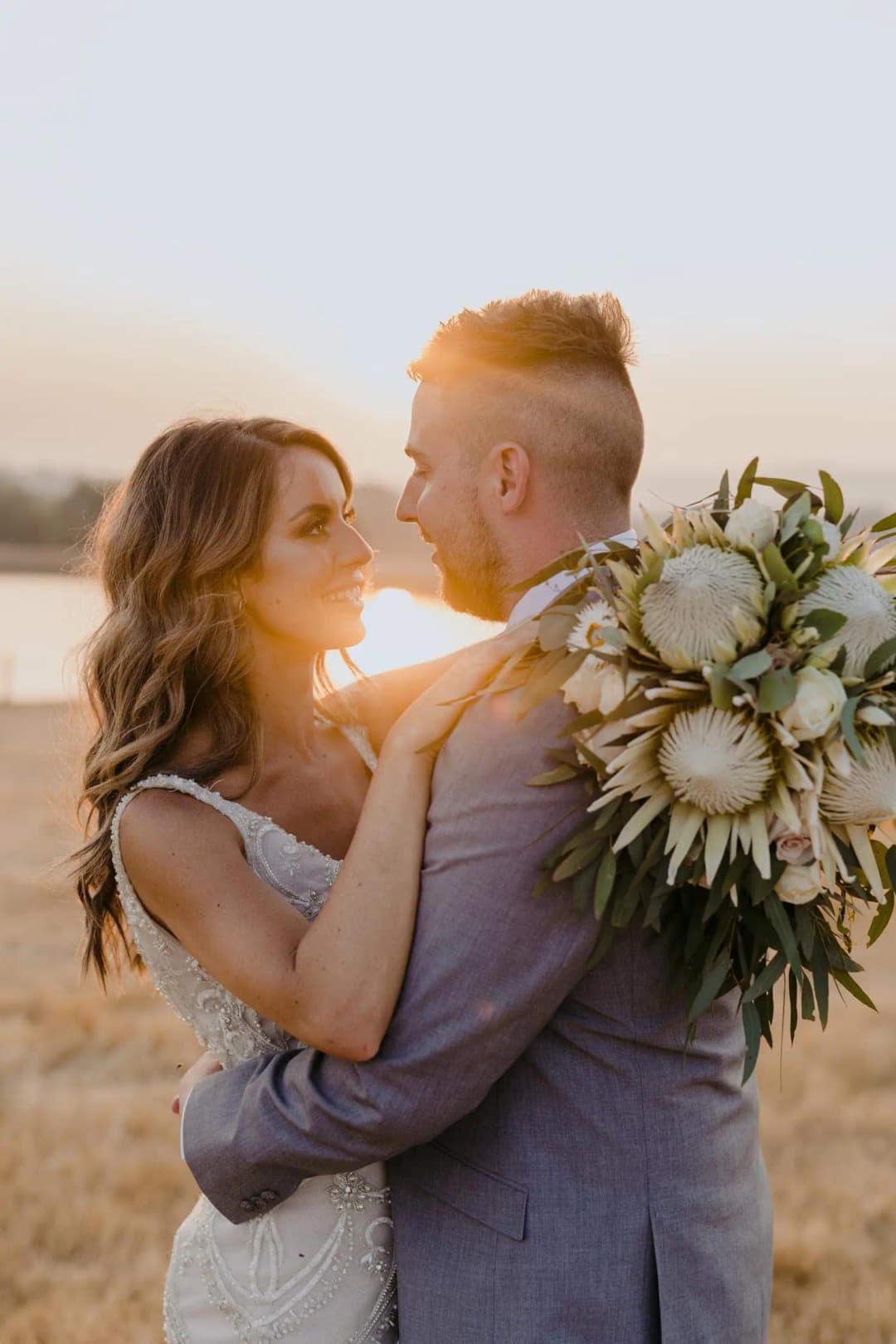 Couple kisses at sunset with the bride's bouquet held behind the groom.