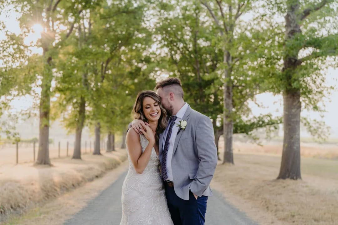 Couple embraces on a tree-lined road in warm evening light.