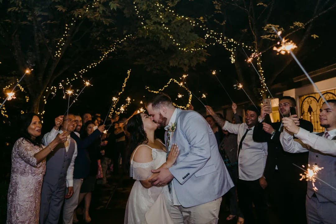 Couple kisses among guests holding sparklers at night.