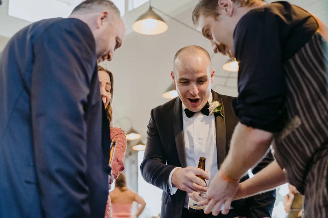 Men react excitedly around a drink being prepared indoors.