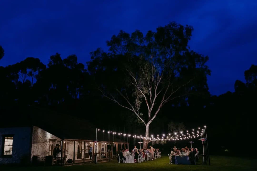 Outdoor reception and string lights beneath trees against a deep blue evening sky.
