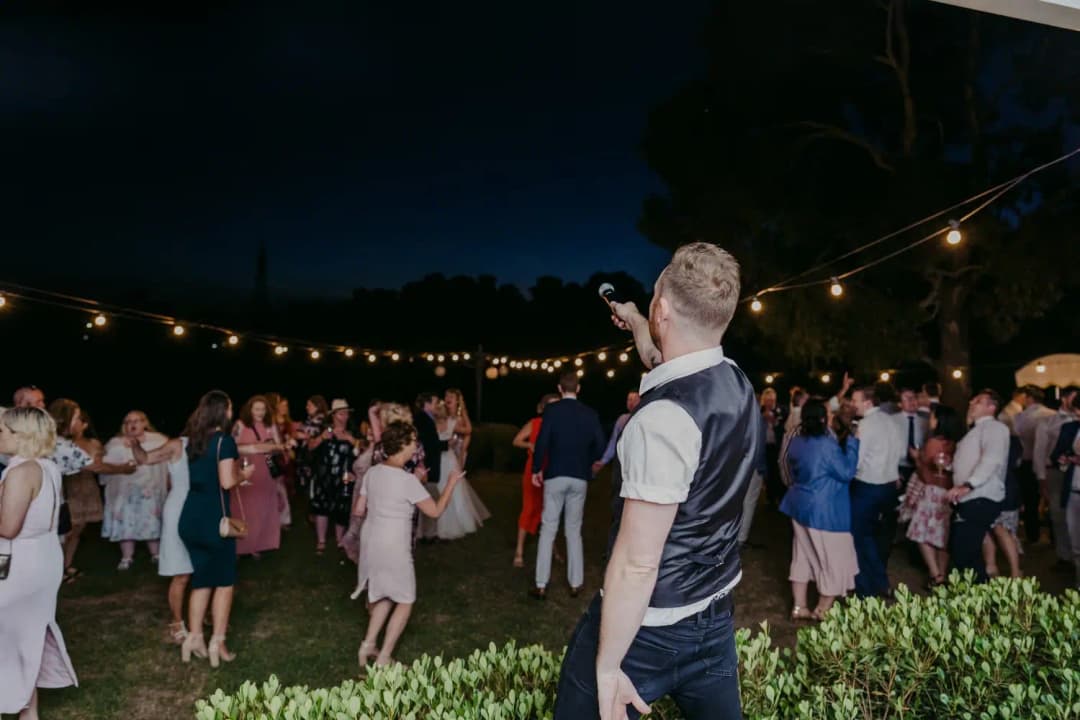 Man raises an arm toward cheering guests on the outdoor dance floor.